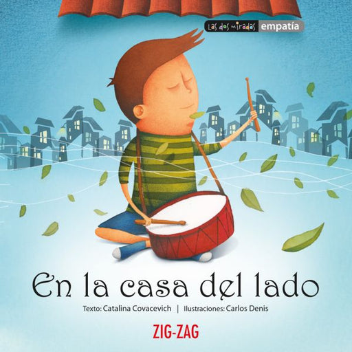 Book cover of En la Casa del Lado with an illustration of a little boy playing a drum with a city scape behind him in the background.