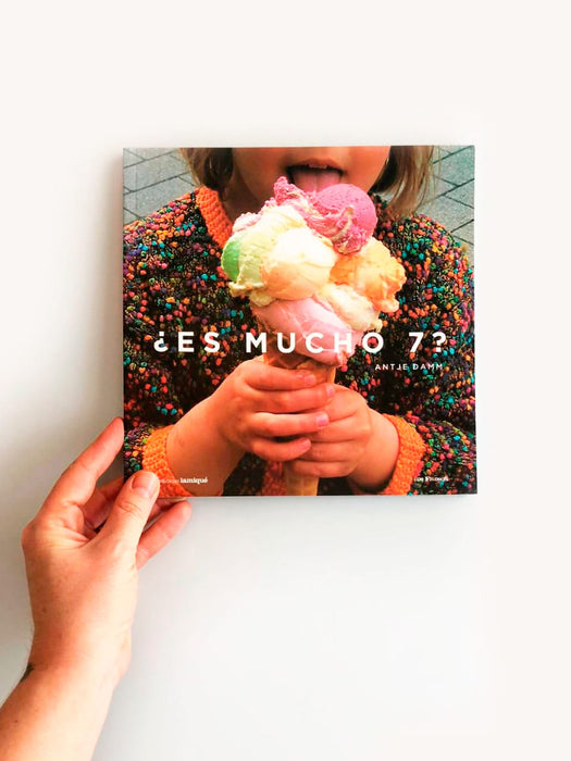 Photograph of someones hand holding the book Es Mucho 7 with a photograph of a child licking an ice cream cone on the cover.